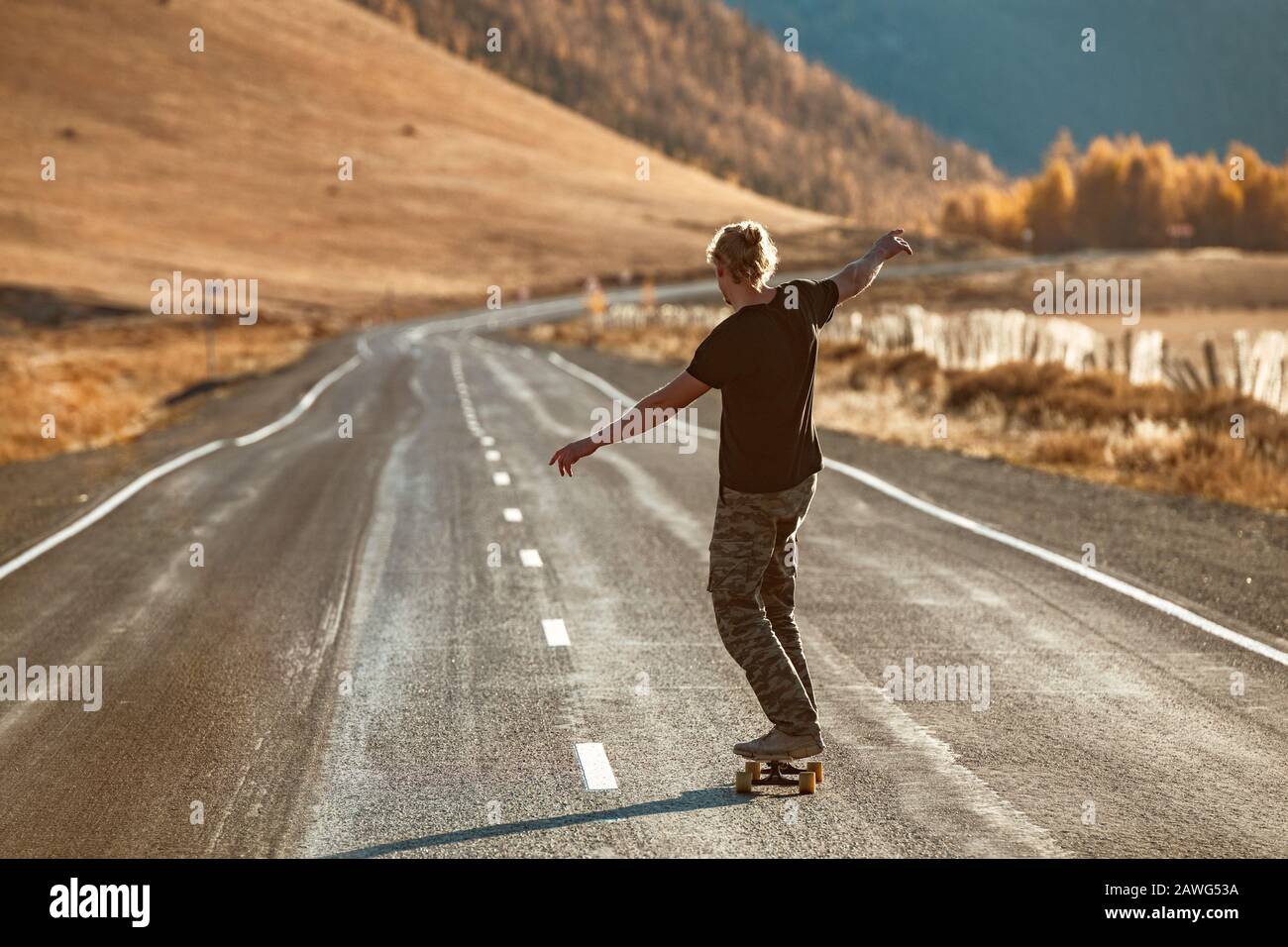 Einsame unerkannte Skateboarder fahren auf Longboard an gerader Bergstraße Stockfoto
