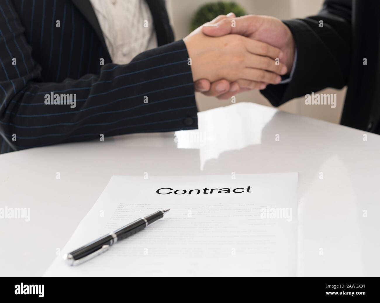 Vertragsabschluss mit Bild eines festen Handshakes zwischen zwei Geschäftspartnern, die einen Vertrag im Hintergrund unterzeichnen. Stockfoto