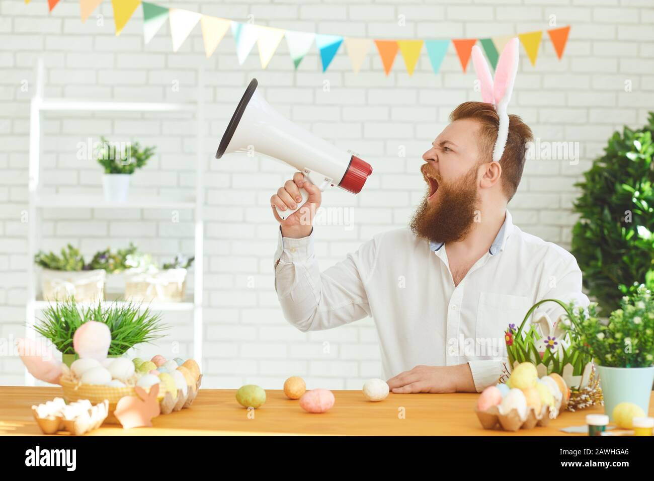 Frohes osterkonzept. Lustiger Mann schreit in einem Megafon vor dem Hintergrund der Osterdekoration. Stockfoto