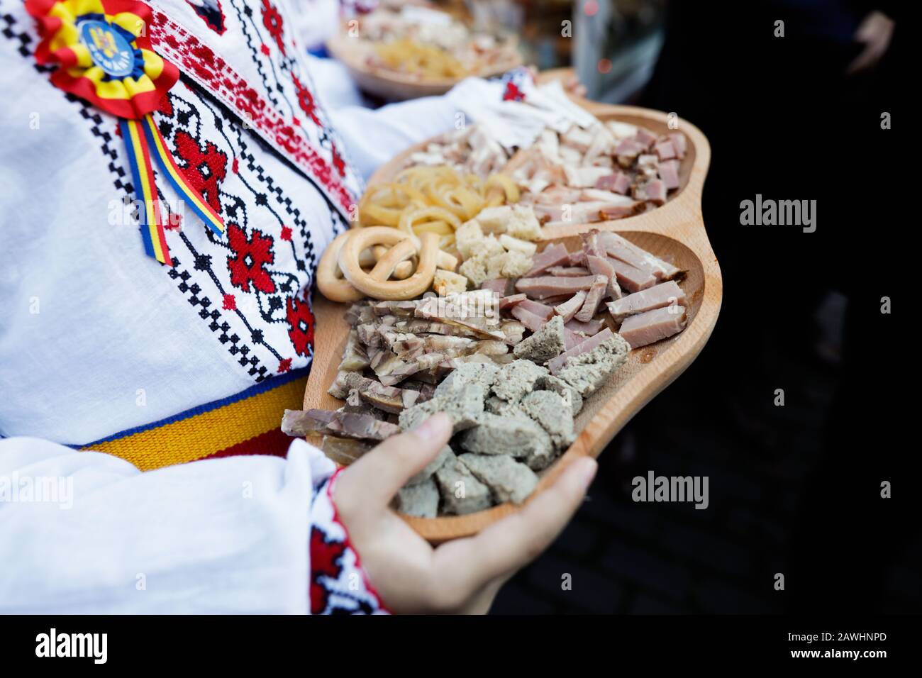 Flache Schärfentiefe (selektiver Fokus) Bild mit einem Jungen, der in traditioneller rumänischer Kleidung gekleidet ist und eine Holzplatte mit verschiedenen Wintergerichten hält, mo Stockfoto