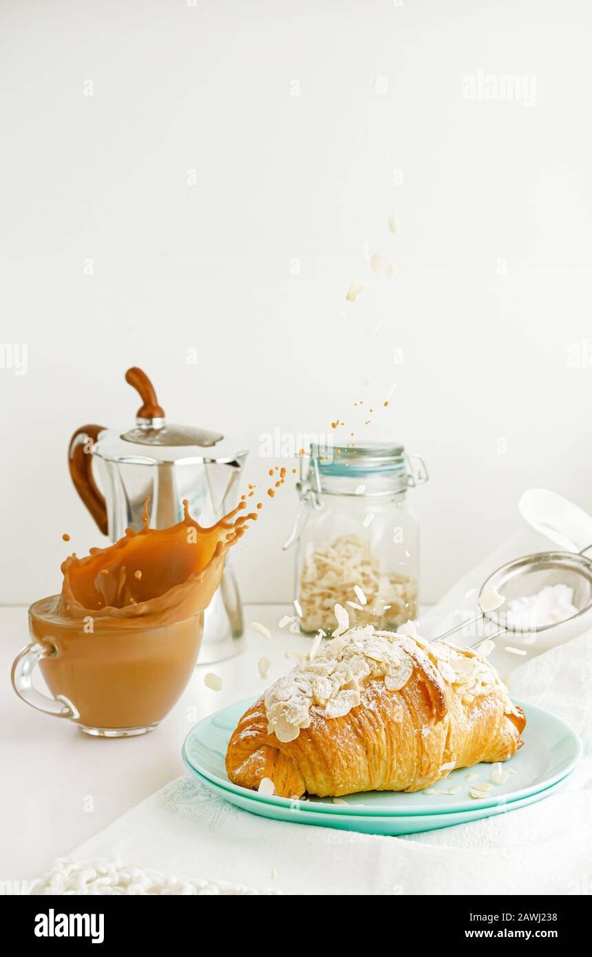 Frühstückstisch. Spritzender Kaffee und herabfallende Mandelflocken auf Croissant. Fliegendes Lebensmittelkonzept. Kopierbereich Stockfoto