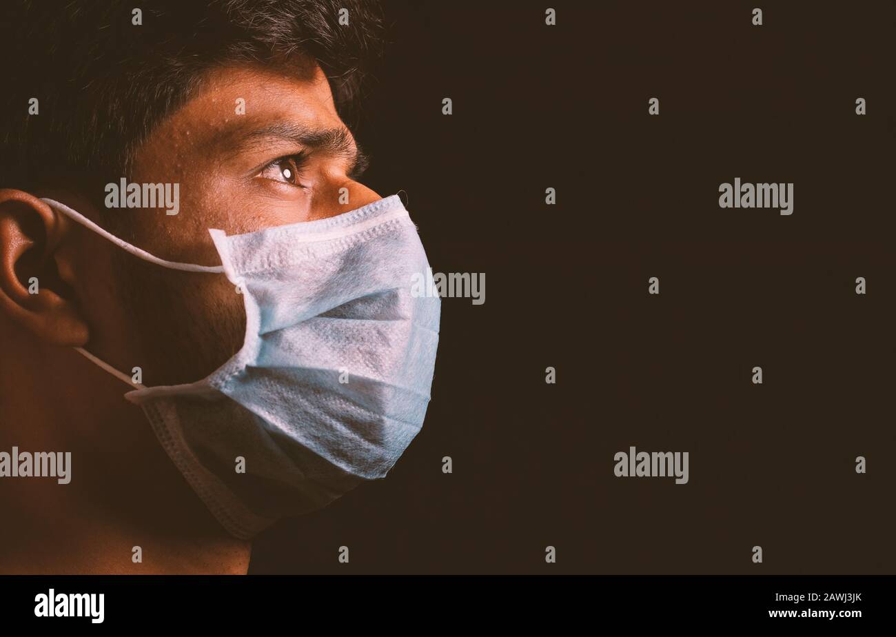 Junger Mann, der eine medizinische Gesichtsmaske trägt, um sich vor der Ausbreitung der Infektion mit dem Coronavirus im dunklen Raum zu schützen und an einen Virusangriff zu denken. Stockfoto