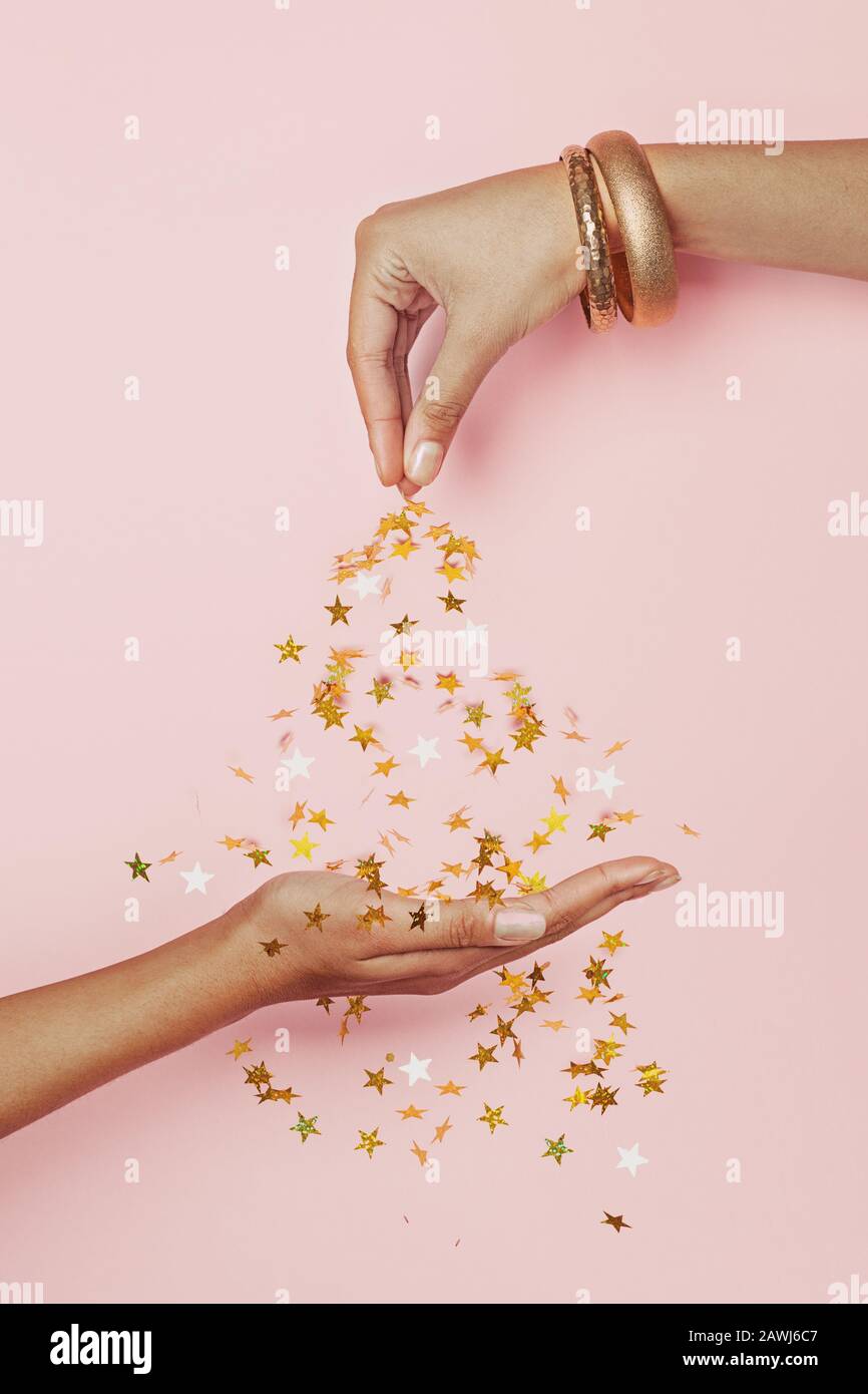 Weibliche Hand bestreut goldene Konfettisterne auf pastellrosa Hintergrund. Feier, Hochzeit, Weihnachten und Geburtstagsfeier Konzept Stockfoto
