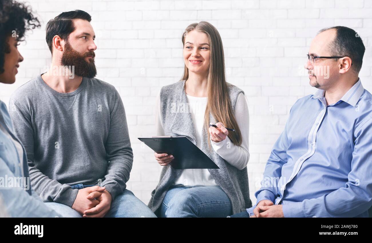 Psychotherapeut spricht während der Gruppentherapiesitzung mit Patienten und nimmt Notizen auf Stockfoto