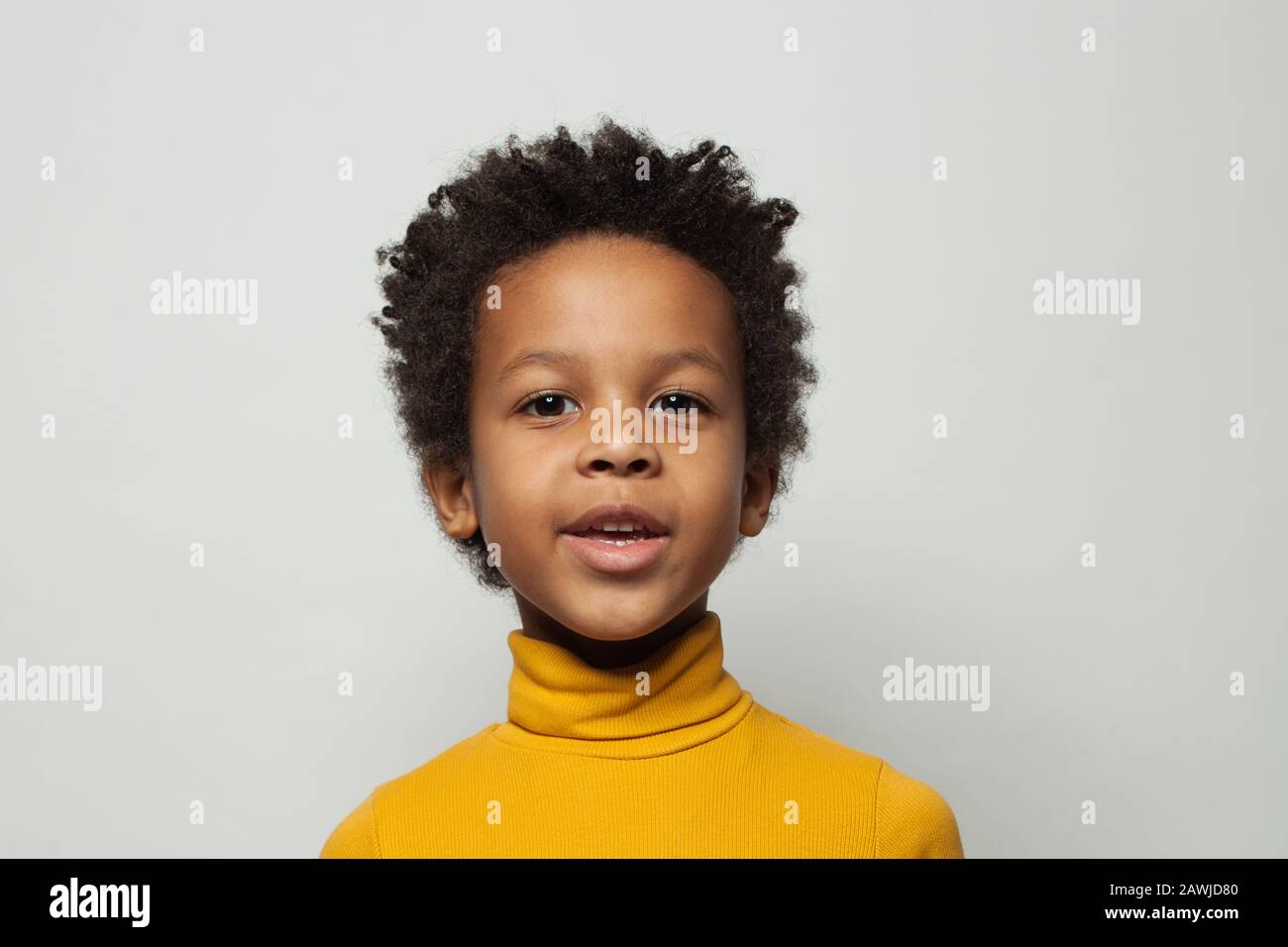 Fröhlicher schwarzer Kinderjunge im gelben Turnleneck-Pullover lächelnd auf weißem Hintergrund Stockfoto