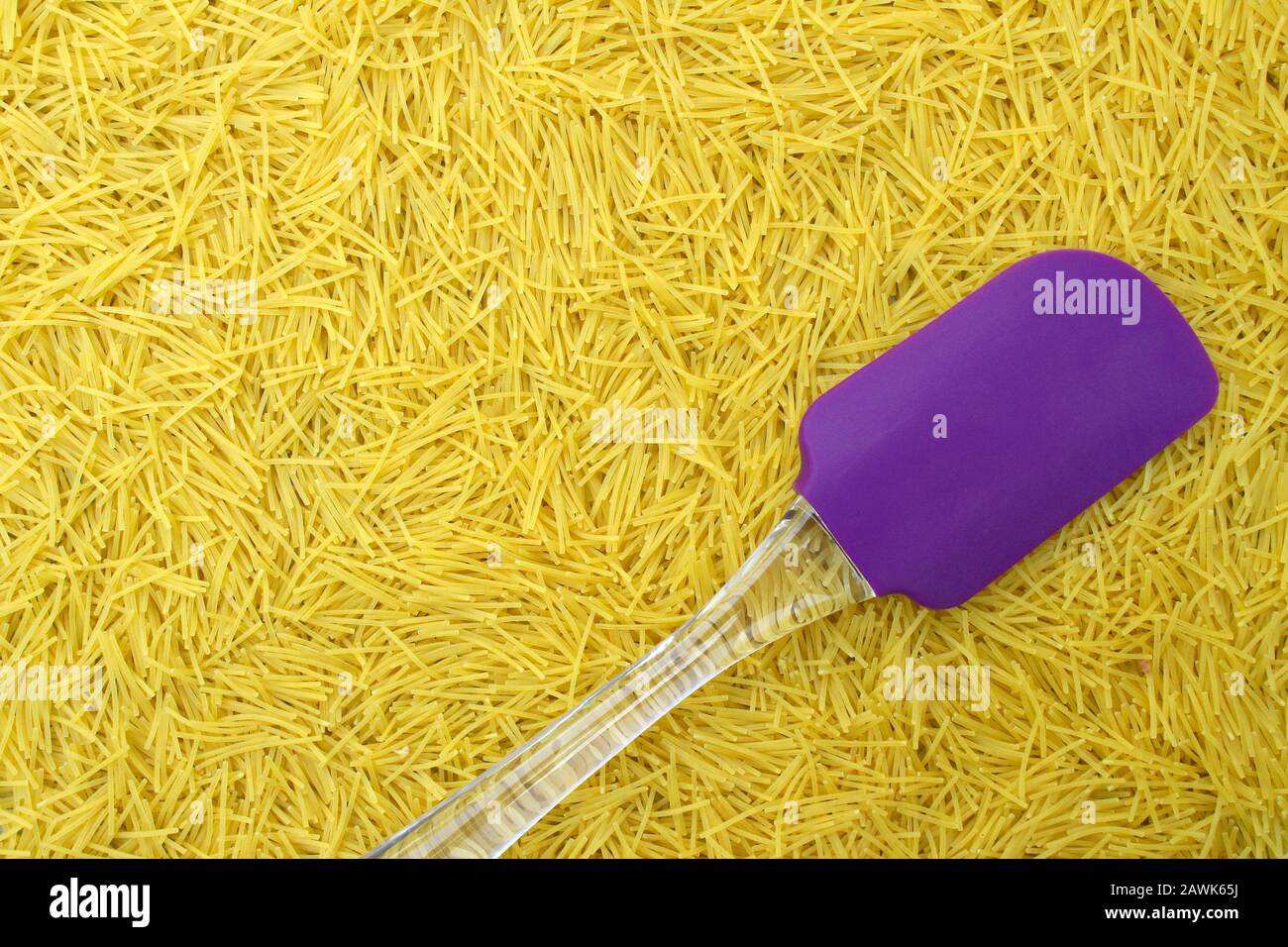 Hintergrund mit italienischem Nudel-Vermicelli und violettem Silikon-Küchenspachtel mit transparentem Griff für Designmenüs oder Lebensmittelrezepte Stockfoto