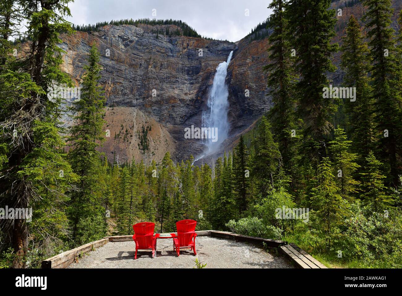 Zwei rote Stühle an einer Unterseite von Takakkaw fallen an einem sonnigen Nachmittag. Takakkaw Falls ist ein Wasserfall im Yoho-Nationalpark in der Nähe Von Field, British CA Stockfoto