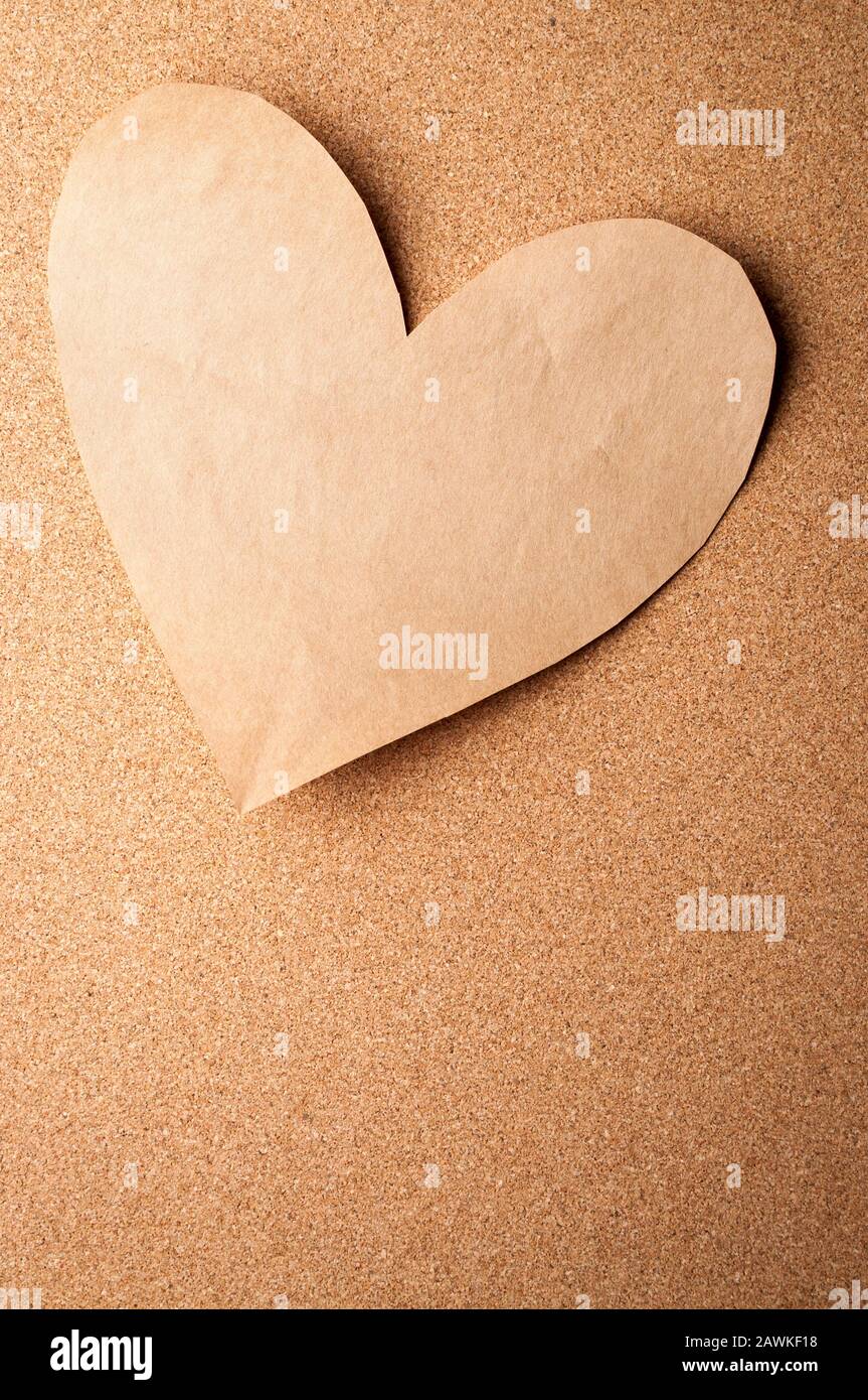 Einfarbiges braunes Papier, Herzausschnitt am Cork Bulletin Board für romantische Valentinstagsnachrichten festgeklemmt Stockfoto