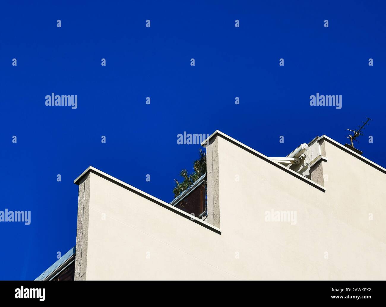Modernes dreigeschossiges Gebäude mit Balkon, Pflanzen und TV-Antenne gegen blauen Himmel. Stockfoto