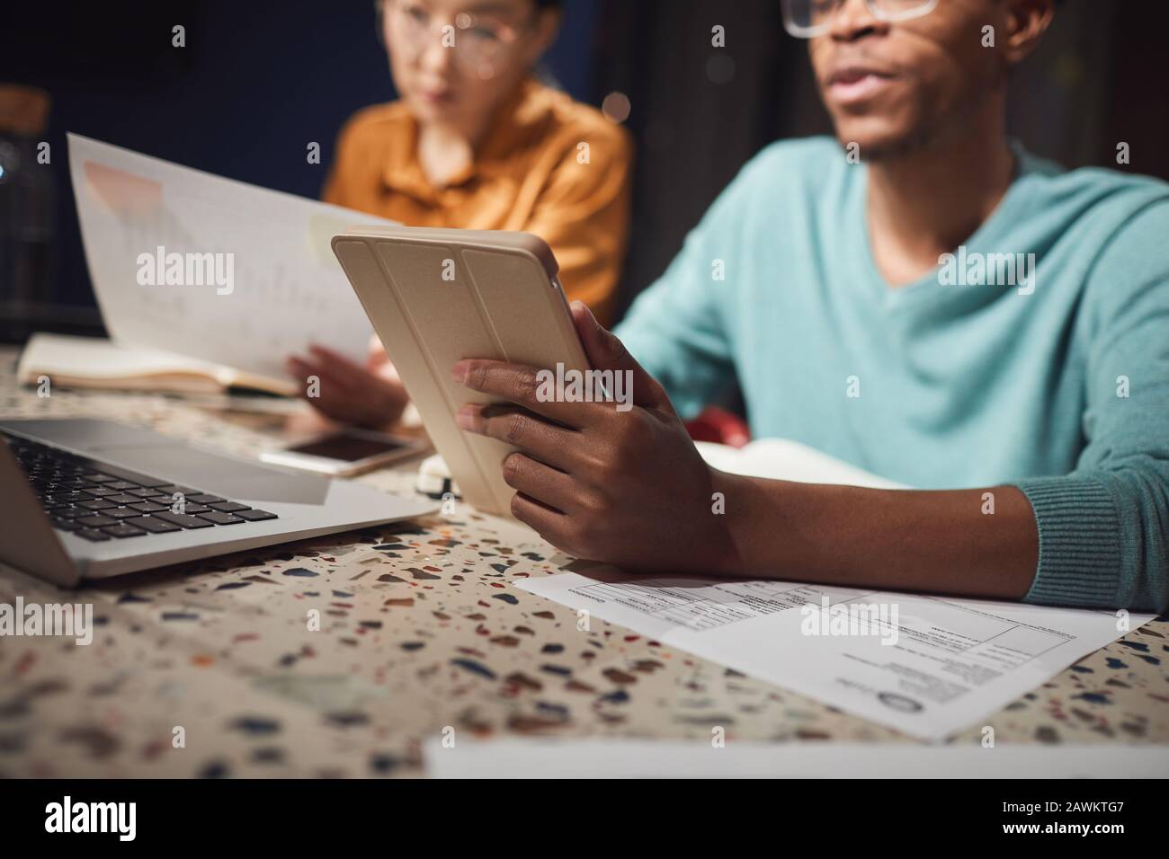 Beschnittenes Porträt zweier ethnischer Geschäftsleute, die spät im dunklen Büro arbeiten, konzentriert sich auf den afrikanischen Mann, der digitales Tablet im Vordergrund hält, den Kopierbereich Stockfoto