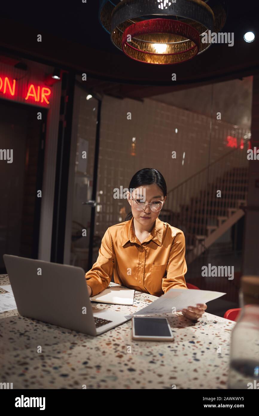 Vertikales Porträt asiatischer Geschäftsfrau mit Laptop bei später Arbeit im dunklen Büro, Kopierraum Stockfoto