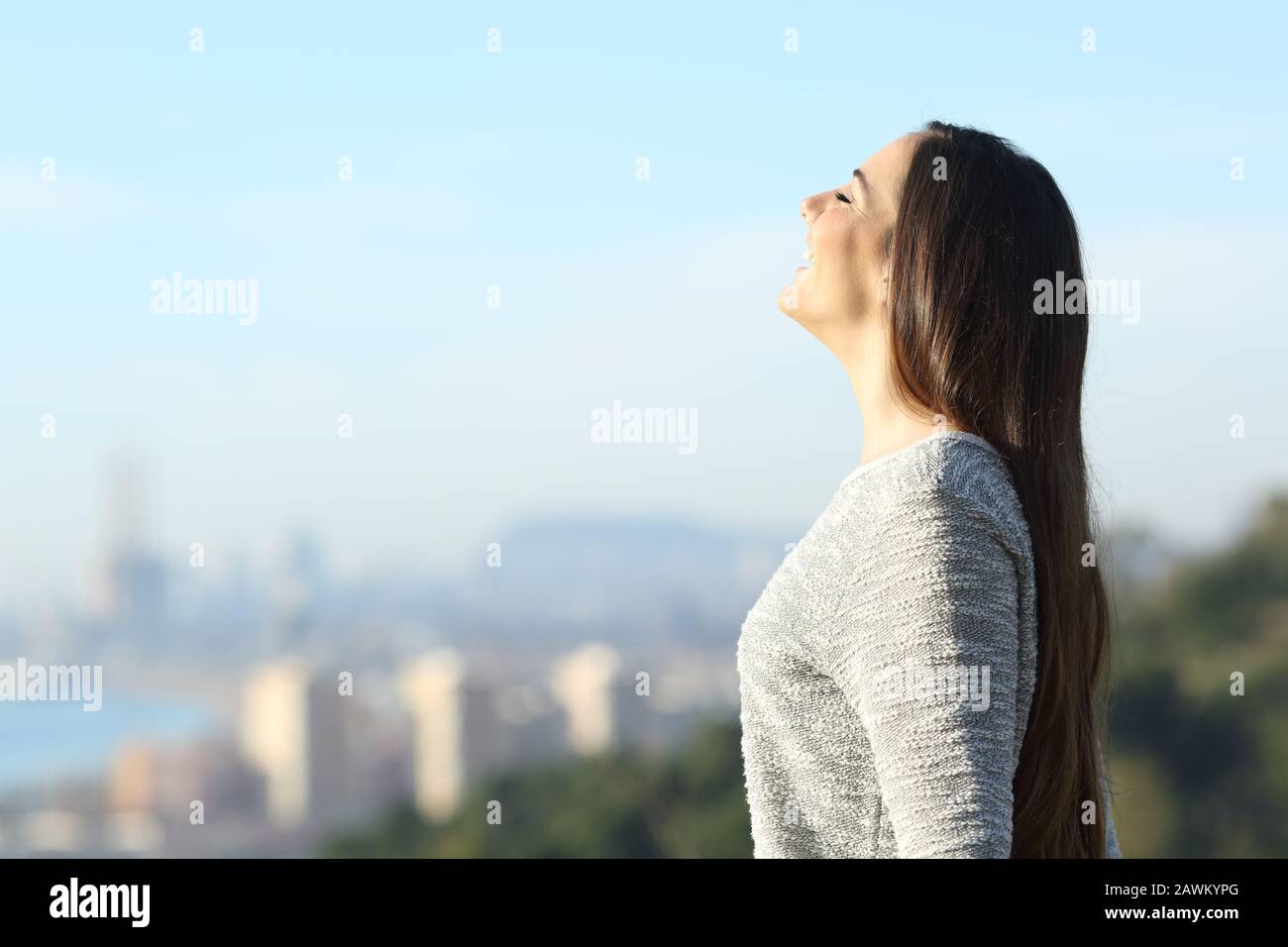 Glückliche Frau atmet frische Luft im Freien mit einer Stadt im Hintergrund einen sonnigen Tag Stockfoto
