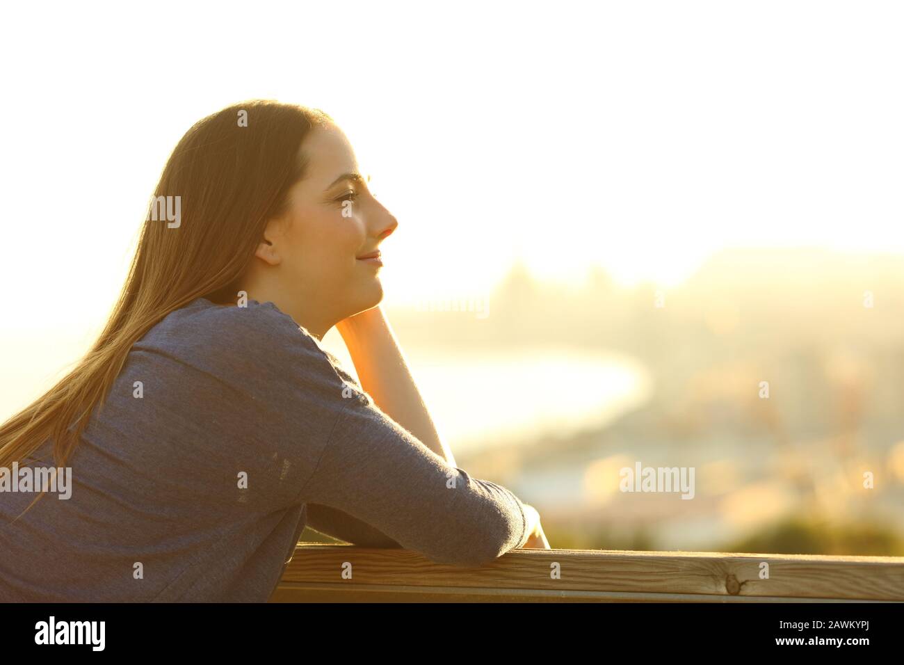 Seitenansicht Portrait einer zufriedenen Frau, die bei Sonnenuntergang von einem Balkon aus eine fantastische Aussicht bietet Stockfoto