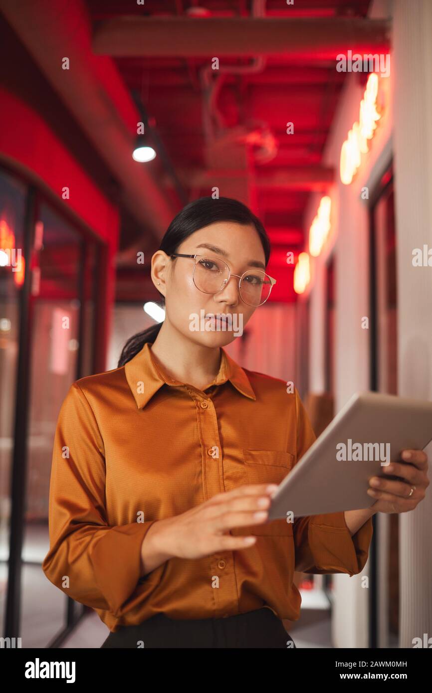 Taille hoch Porträt der modernen asiatischen Geschäftsfrau, die Tablet hält und Kamera beim Aufstellen im Freien betrachtet Stockfoto