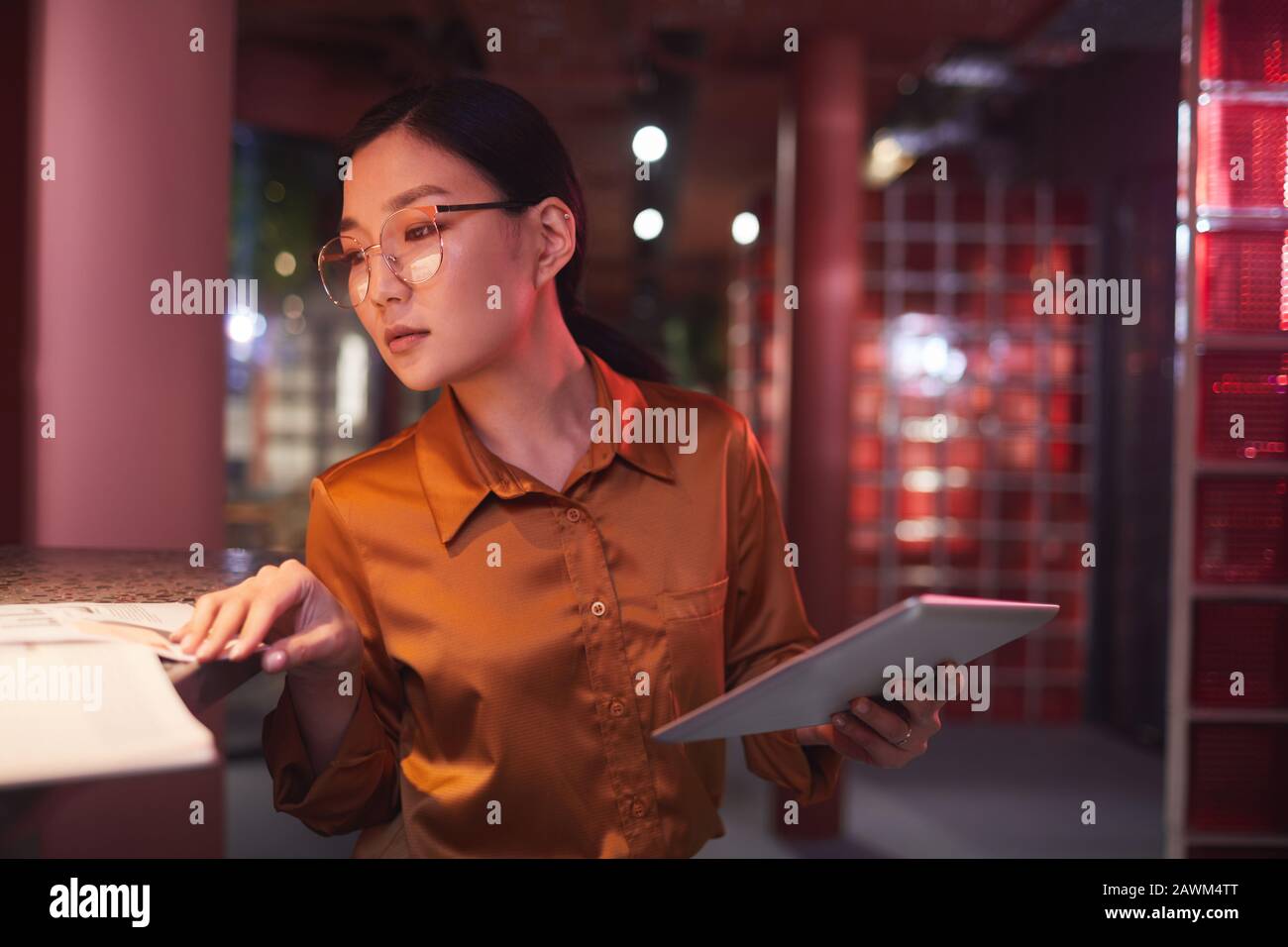 Taillen-Up-Portrait zeitgenössischer asiatischer Geschäftsfrau mit digitalem Tablet, während sie in futuristischem Büro-Interieur und im Kopierbereich arbeitet Stockfoto