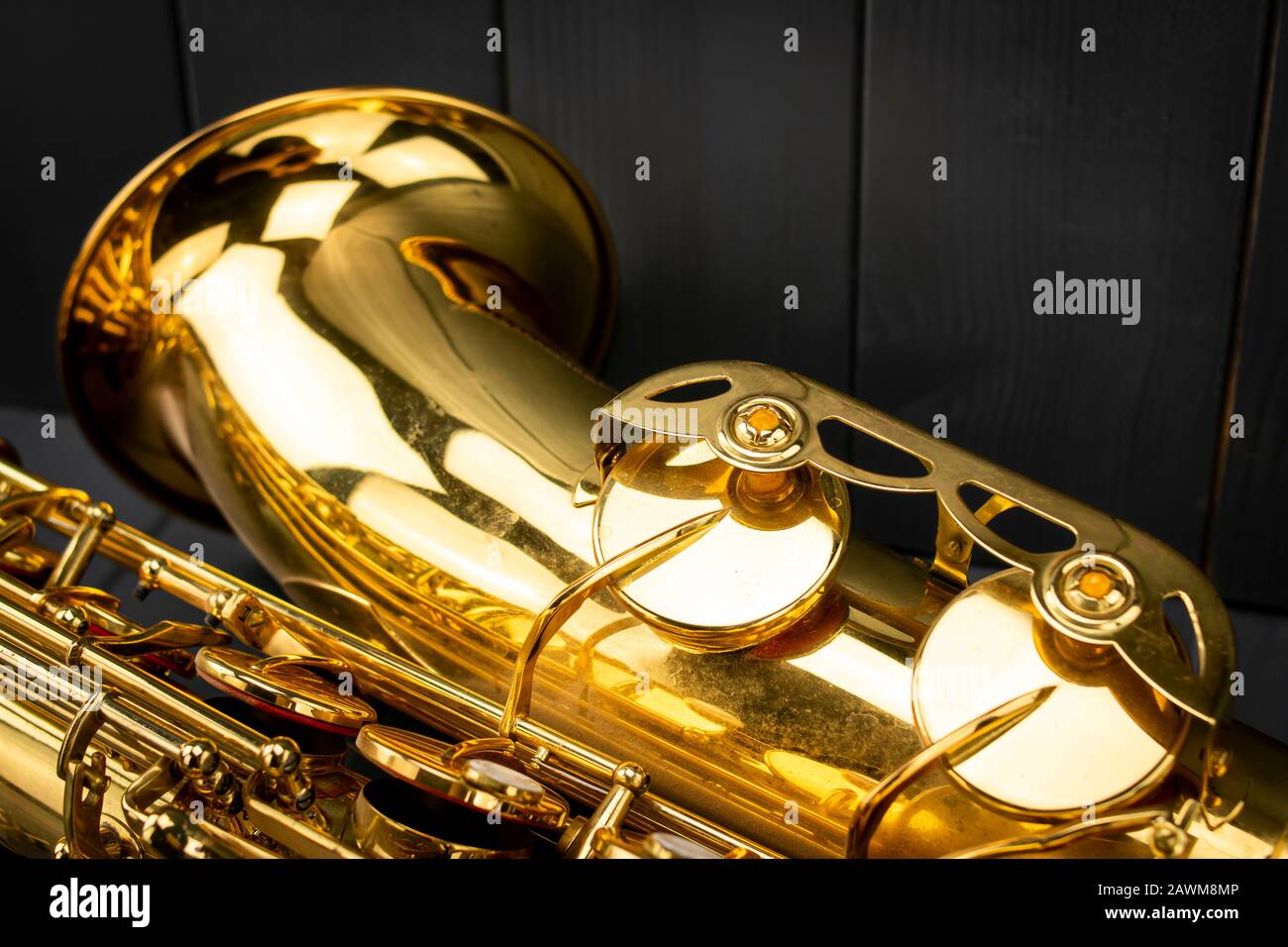 Die Glocke und einige Noten Tasten eines Tenorsaxophons im Vordergrund auf grauem Holzhintergrund Stockfoto