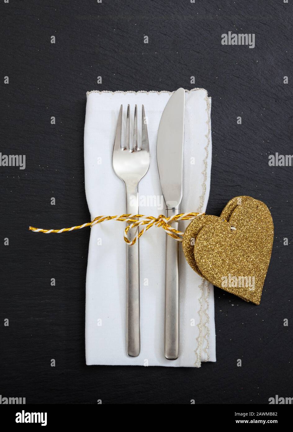 Valentinstagssesstisch. Gabel- und Messerbesteck, weiße Serviette und goldene Farbherzen auf schwarzem Hintergrund, Draufsicht. Stockfoto