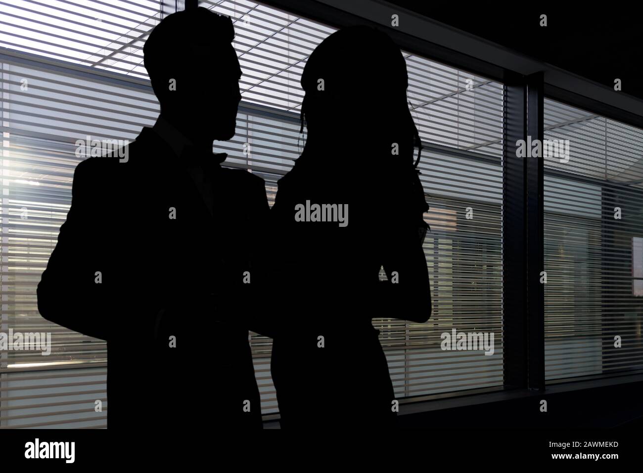 Konzeptbild der Romantik bei der Arbeit - Silhouetten einer Frau und eines Mannes, der sich in einem dunklen Büro umarmt Stockfoto