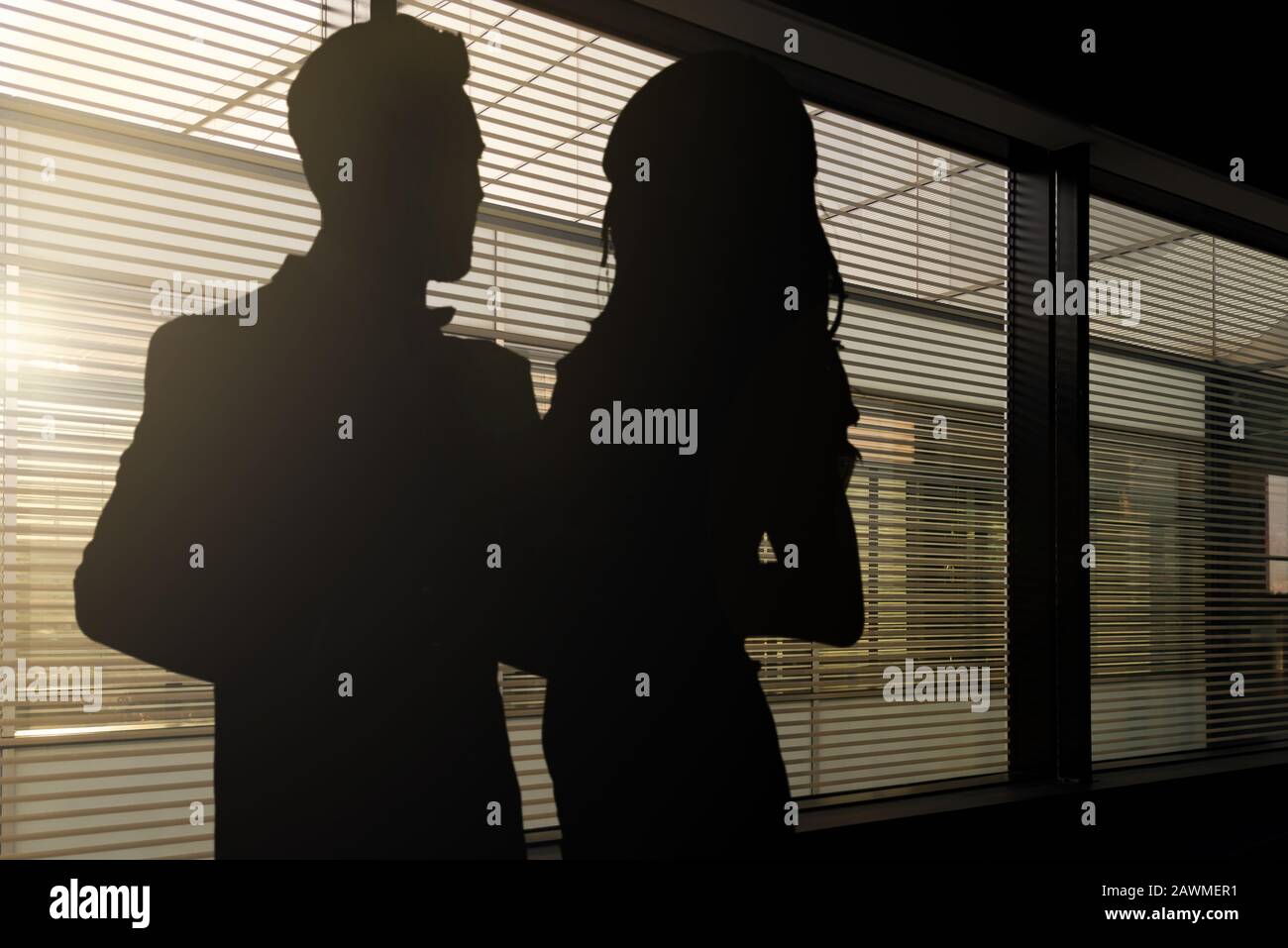 Konzeptbild der Romantik bei der Arbeit - Silhouetten einer Frau und eines Mannes, der sich in einem dunklen Büro umarmt Stockfoto