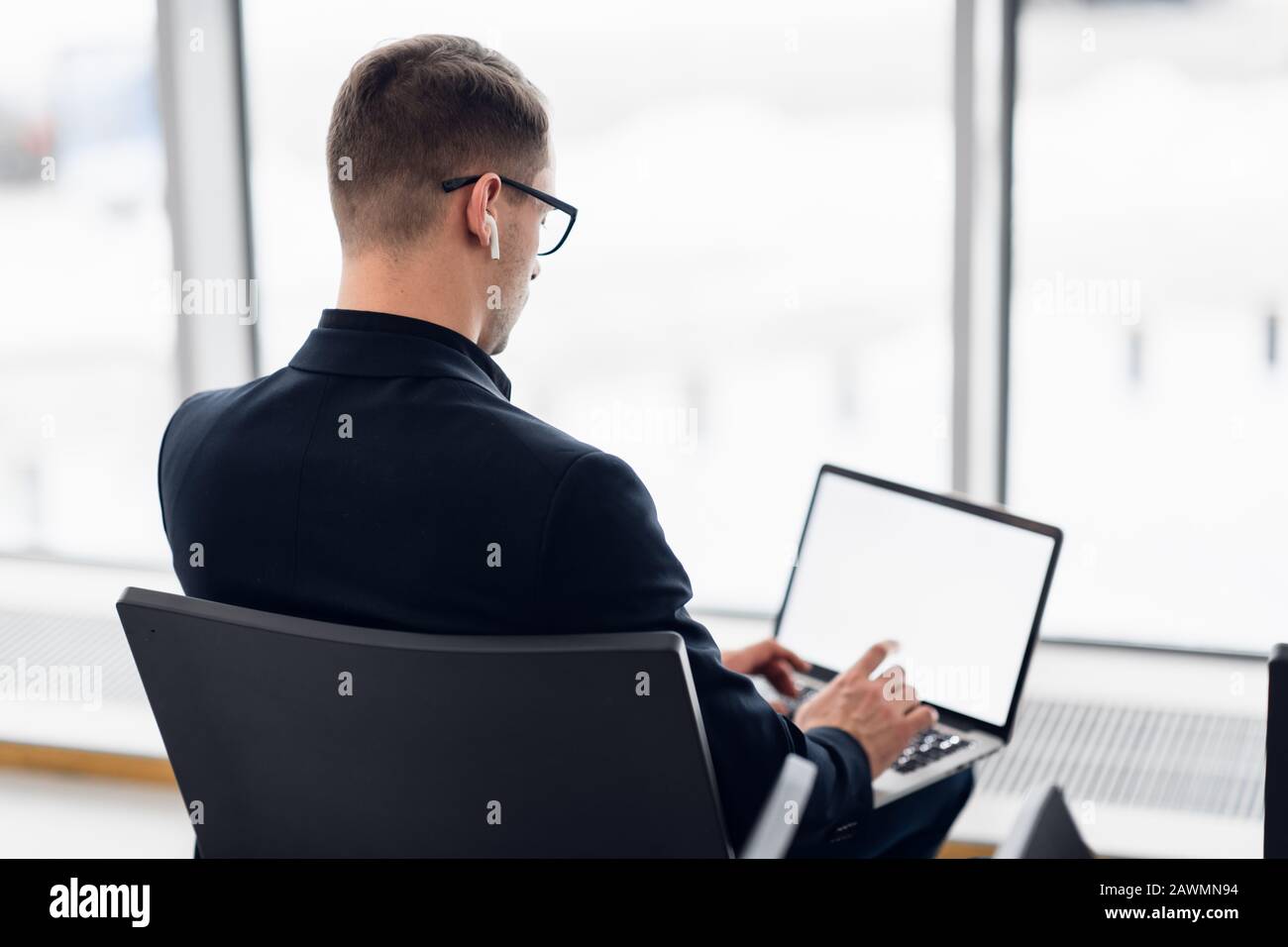Junger Geschäftsleute, der auf dem Computer am Flughafen sitzt und auf den Flug wartet. Ansicht von hinten Stockfoto