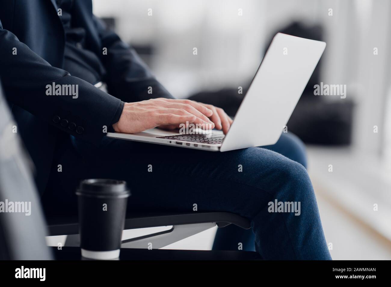 Junger Geschäftsleute, der auf dem Computer am Flughafen sitzt und auf den Flug wartet. Nahansicht von der Seite Stockfoto