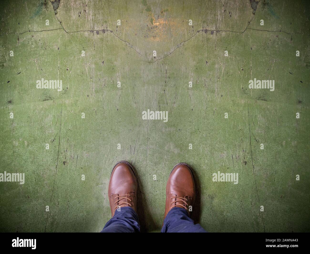 High-Angle-Aufnahme einer Person mit braunen Schuhen an Eine verwitterte grüne Oberfläche Stockfoto