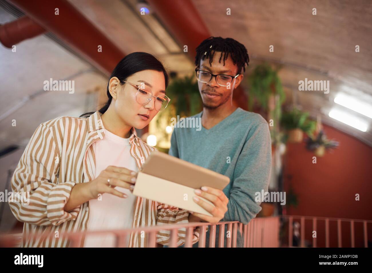 Taille up Portrait der asiatischen jungen Frau mit digitalem Tablet, während Sie mit Kollegen im modernen Büro über ein Arbeitsprojekt diskutieren, Kopierer Stockfoto