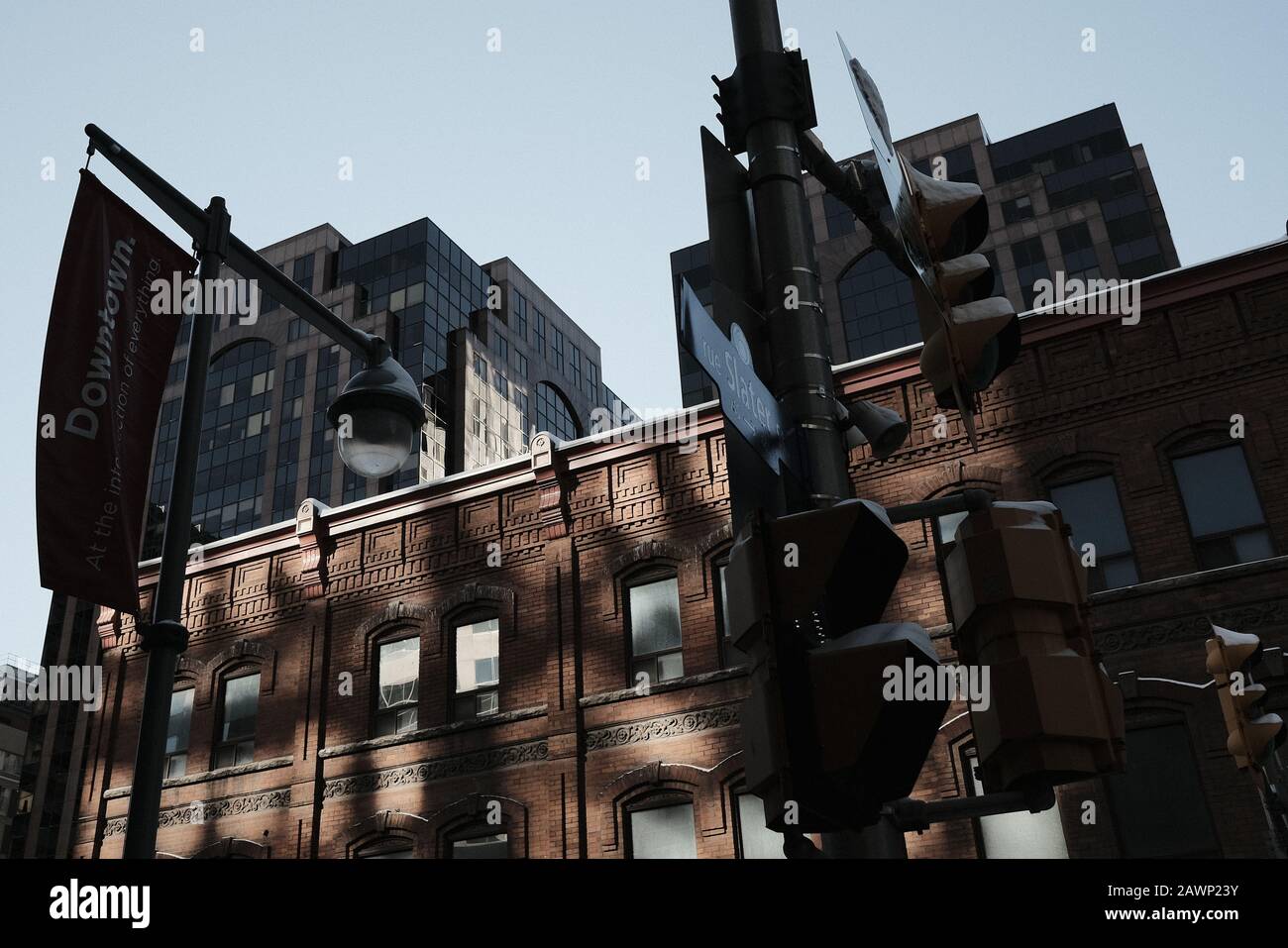 Reflektierte Sonne beleuchtet ein brauner Ziegelbau in der Innenstadt von Ottawa, mit Bürohochhäusern im Hintergrund und Ampeln im Vordergrund. Stockfoto