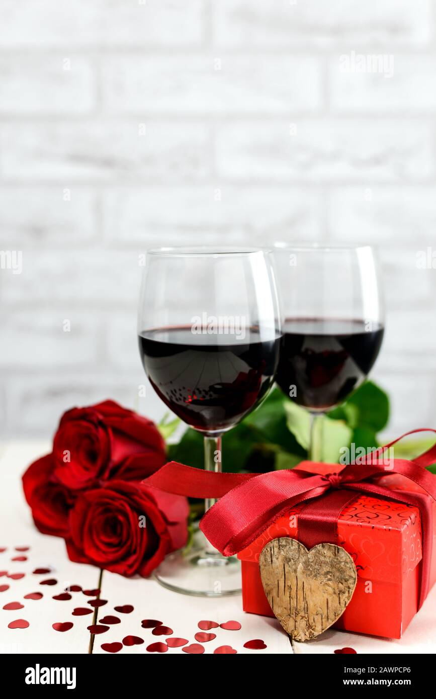 Valentinstag Konzept. Zwei Gläser Wein, rote Rosen, Geschenkbox und Holzherz auf einem weißen Holztisch. Selektiver Fokus. Stockfoto