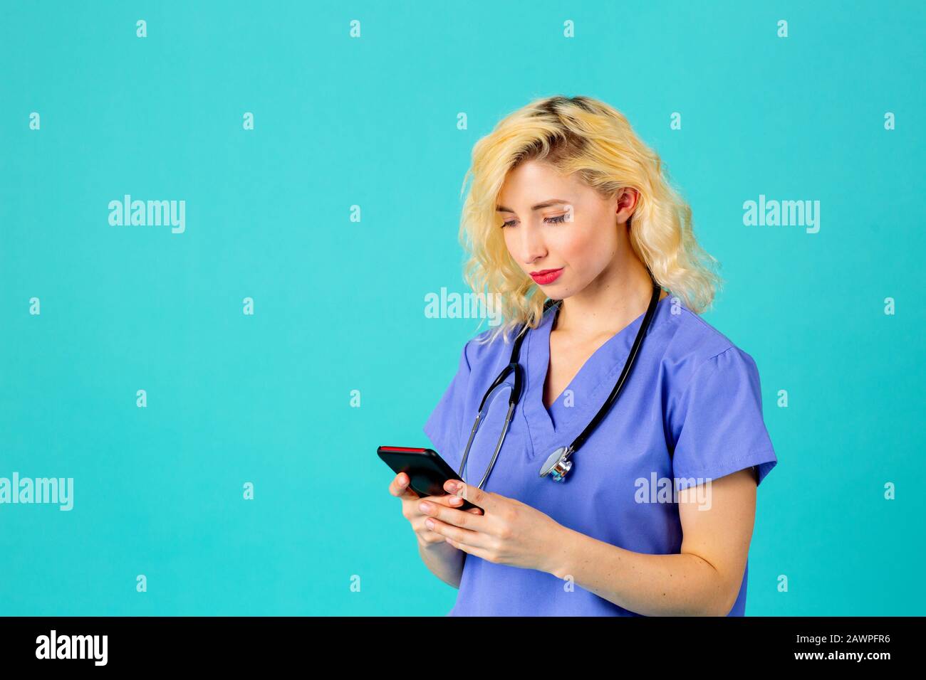 Studioporträt einer jungen Ärztin oder Krankenschwester, die mit ihrem Handy eine blaue Schrubbbensuniform und ein Stethoskop trägt Stockfoto