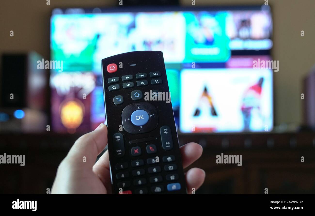 Weibliche Hand, die eine Smart tv-Fernbedienung hält und auf den fernseher zeigt und Programme auswählt Stockfoto