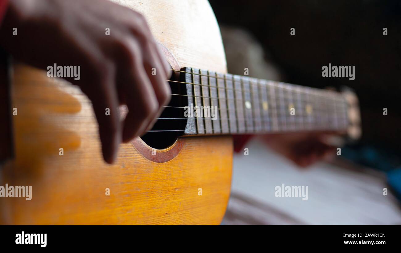 Der Kerl spielt Gitarre, gelbes Musikinstrument aus Holz, der Mann iteriert über die Saiten einer akustischen Gitarre. . Stockfoto
