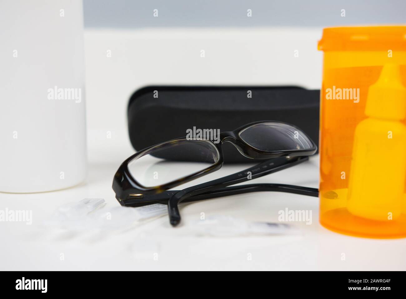 Brille neben verschreibungspflichtigen Fläschchen, Brillenetui, Augentropfer und Lösungsflasche. Weißer Badezimmertisch Stockfoto