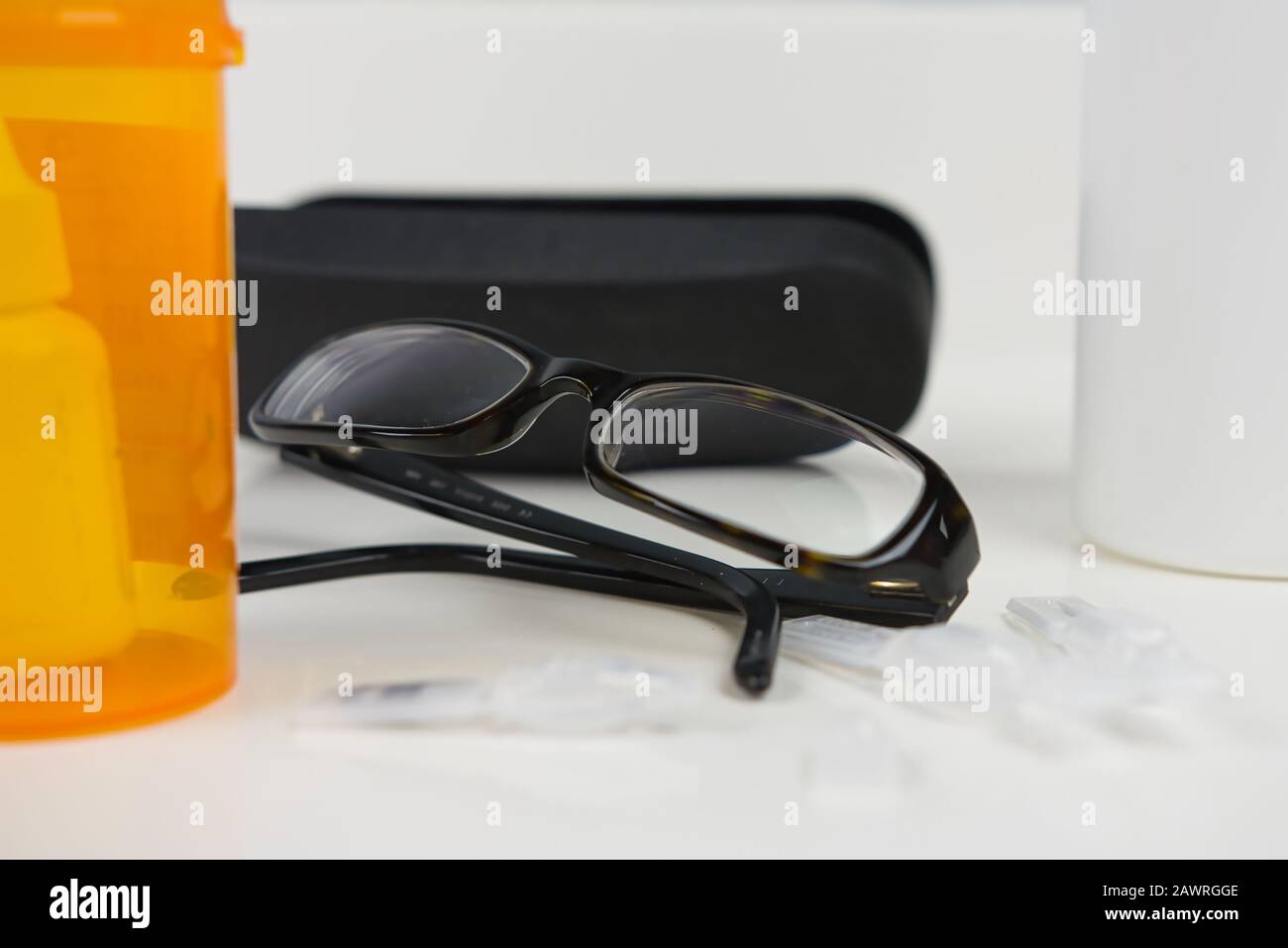 Brille neben verschreibungspflichtigen Fläschchen, Brillenetui, Augentropfer und Lösungsflasche. Weißer Badezimmertisch Stockfoto