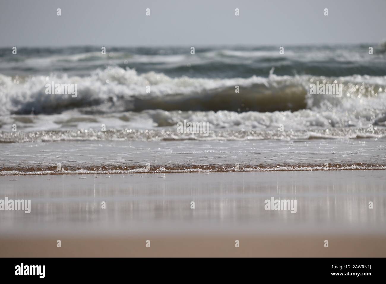 Brillanter Schuss von großer Meereswasserwelle am Strand gegen blauen Himmel mit Sandvordergrund, Strandlandschaft Stockfoto