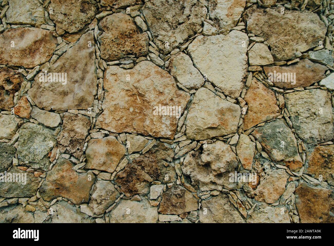 Die Wand aus grauem und braunem Naturstein ist in Form von Ziegelsteinen mit kleinen Felsen dazwischen ausgelegt. Stockfoto