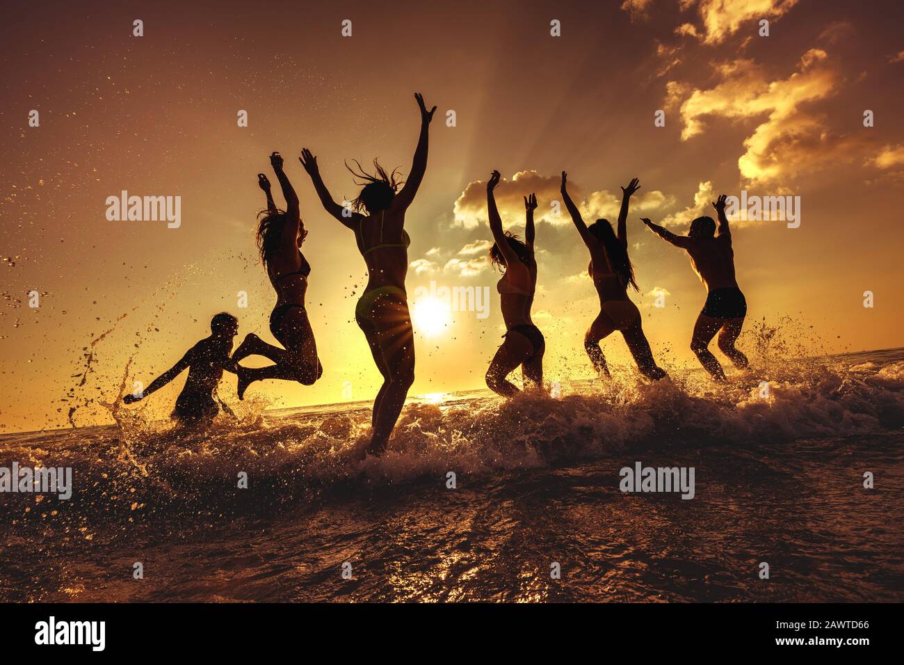 Eine große Gruppe glücklicher junger Freunde macht Spaß am Meeresstrand bei Sonnenuntergang, läuft und springt über Wellen Stockfoto