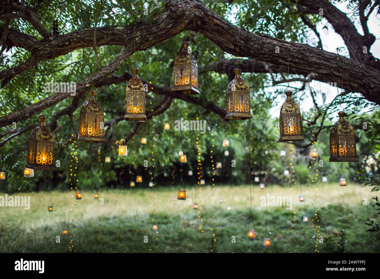 Abendhochzeit mit vielen alten Laternen, Lampen und Kerzen. Ungewöhnliche Dekoration im Freien. Schönes Gartenparty-Konzept. Stockfoto