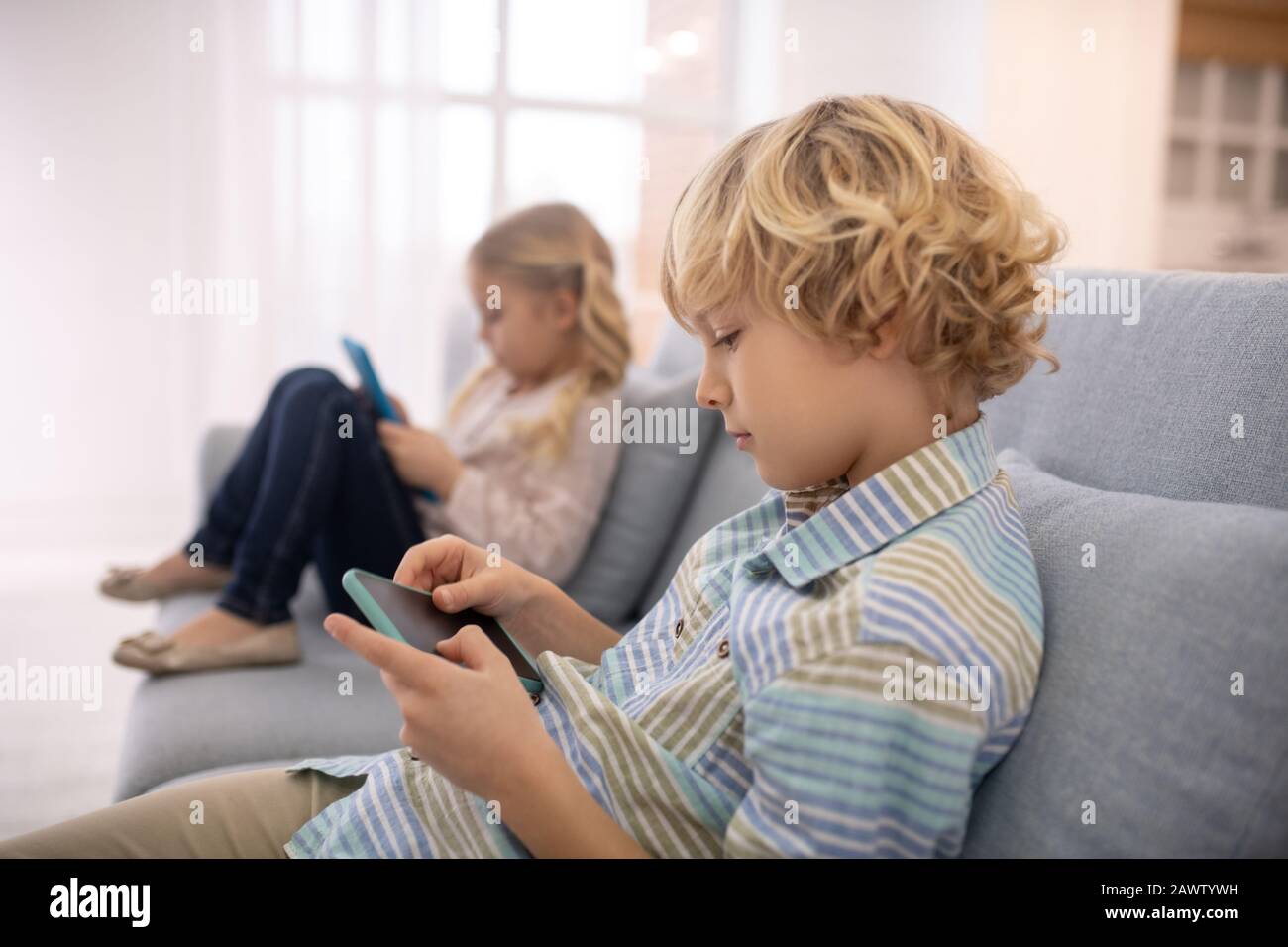 Junge und Mädchen sitzen auf dem Sofa und spielen mit Gadgets Stockfoto