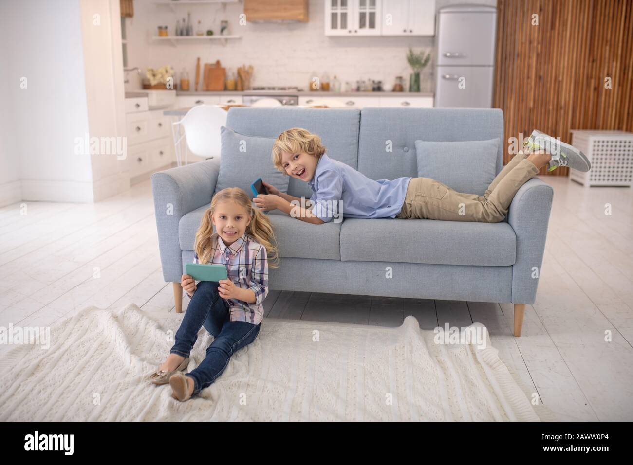 Junge auf dem Sofa liegend, Mädchen mit Gadgets auf dem Boden sitzend Stockfoto