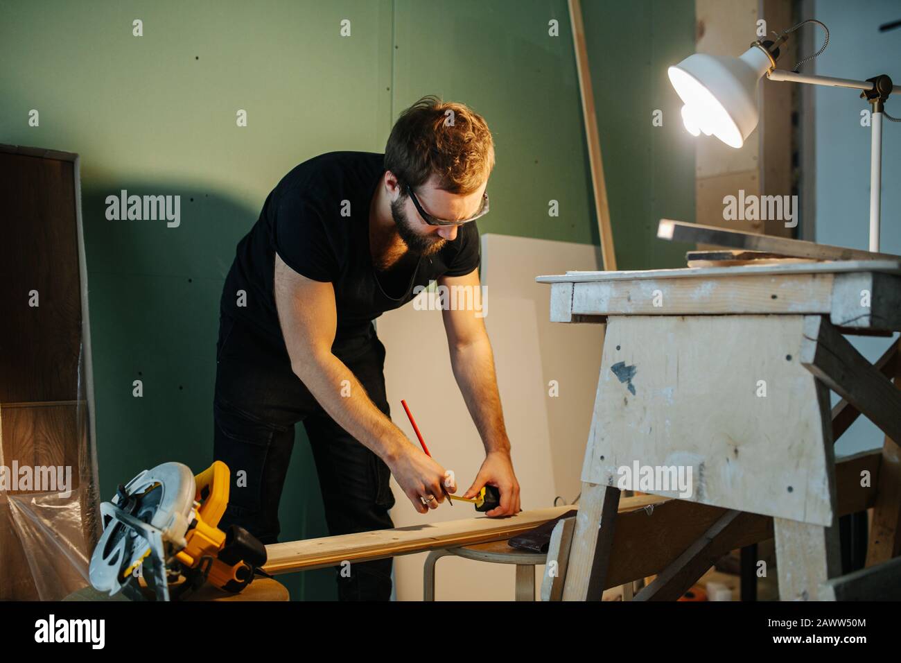 Mann, der an der Renovierung seiner Wohnung arbeitet. Messplanke mit einem Bandmessgerät. Stockfoto