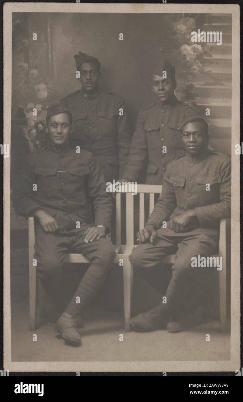 Vier nicht identifizierte afroamerikanische Soldaten in Uniformen und Überseekappen vor bemalter Kulisse Stockfoto