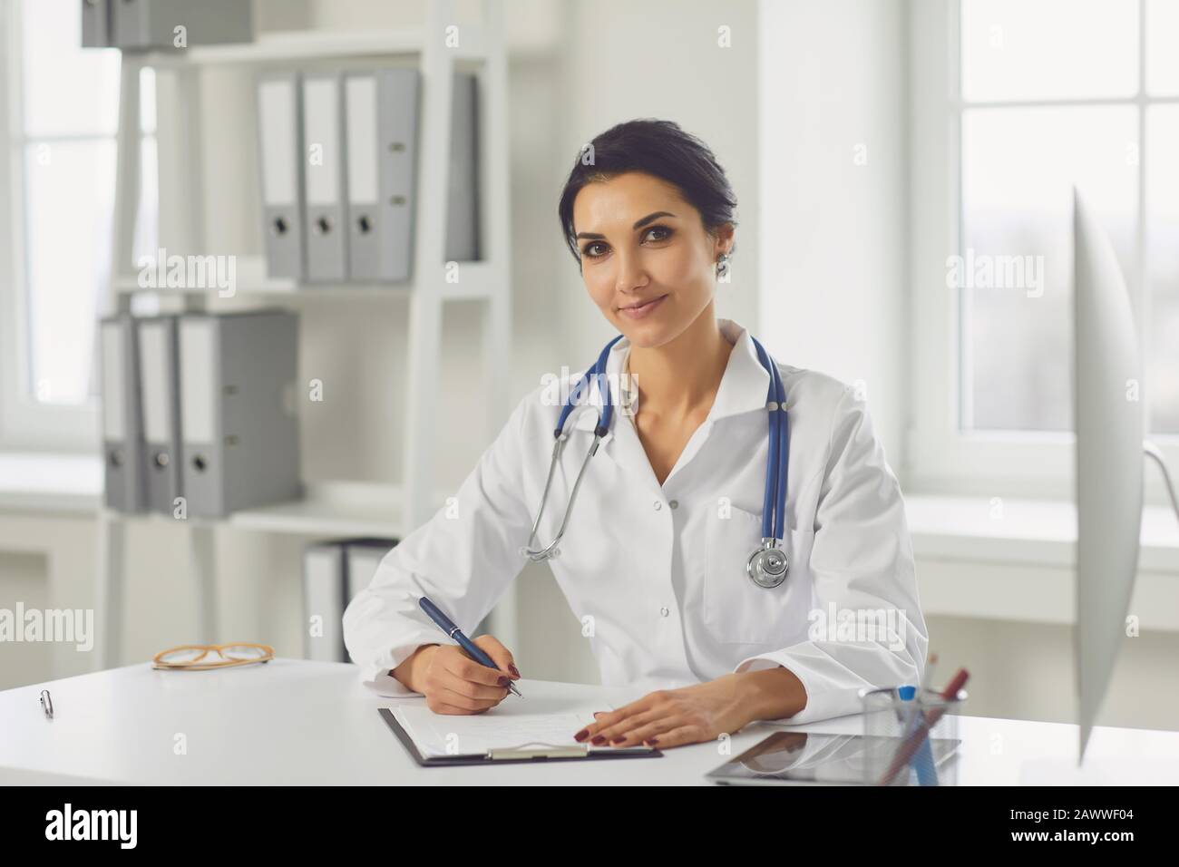 Selbstbewusste Frau Ärztin Kinderärztin schreibt in einer Zwischenablage, die an einem Tisch in einem weißen Büro des Krankenhauses sitzt Stockfoto