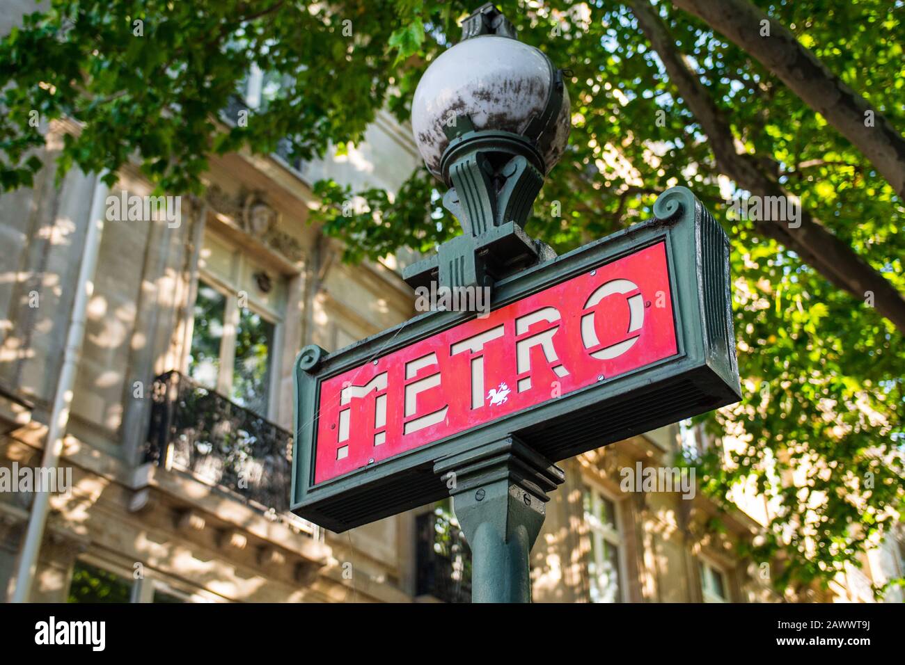 Schönes typisches rotes U-Bahn-Schild (Paris, Frankreich). Europäischer Stil, Aufnahmen im niedrigen Winkel mit verschwommenem Naturhintergrund. Straßenelement aus grünem Stahl Stockfoto