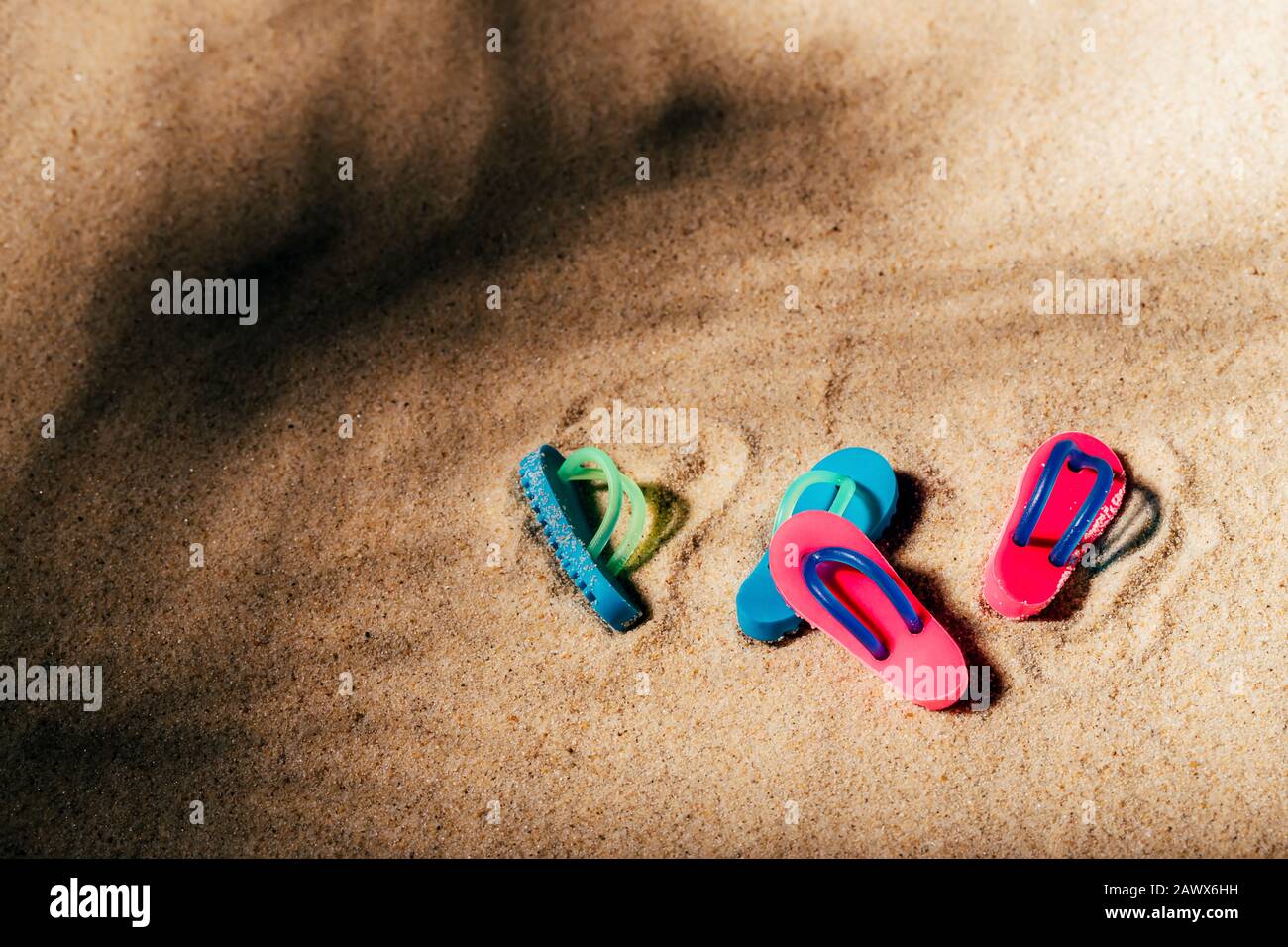 Zwei Paar Strandsandalen oder Dongs an einem sandigen Strand unter dem Palmenschatten. Hintergrund mit freiem Kopierspeicher. Stockfoto