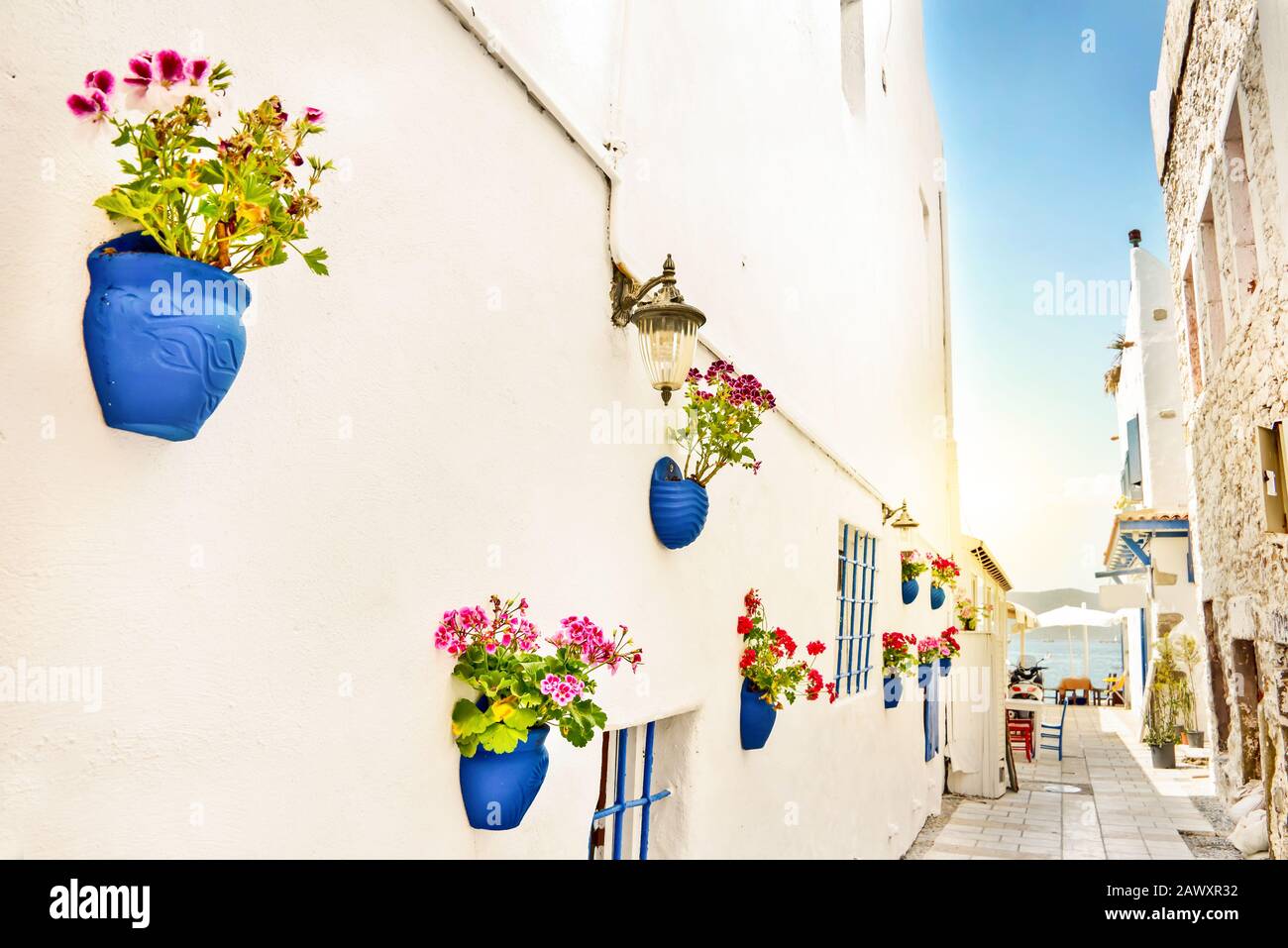 Eine enge Straße mit Whote-Wänden und blauen Blumentöpfen, das mittelmeer im Hintergrund, Bodrum, Türkei Stockfoto