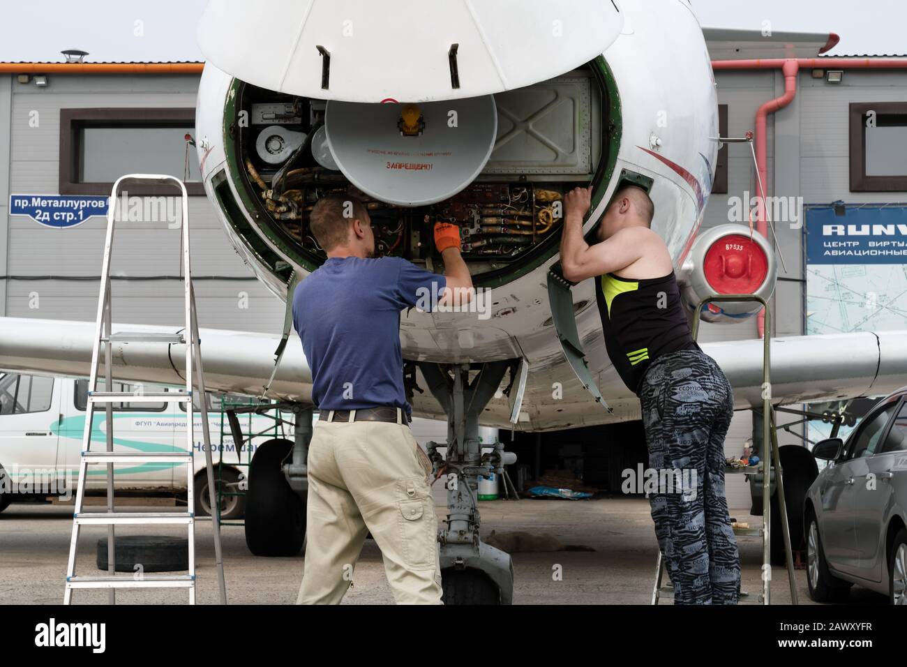 Flugzeugmechaniker reparieren einen Flugzeugmotor direkt auf dem Parkplatz unter den Autos, eine ungewöhnliche Situation. Stockfoto