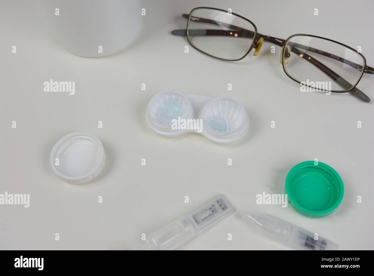 Flache Lay verschiedener Augenpflegeprodukte auf weißem Counter. Kontaktlinsengehäuse mit Brille, Paprika und Lösungsumgebung geöffnet Stockfoto
