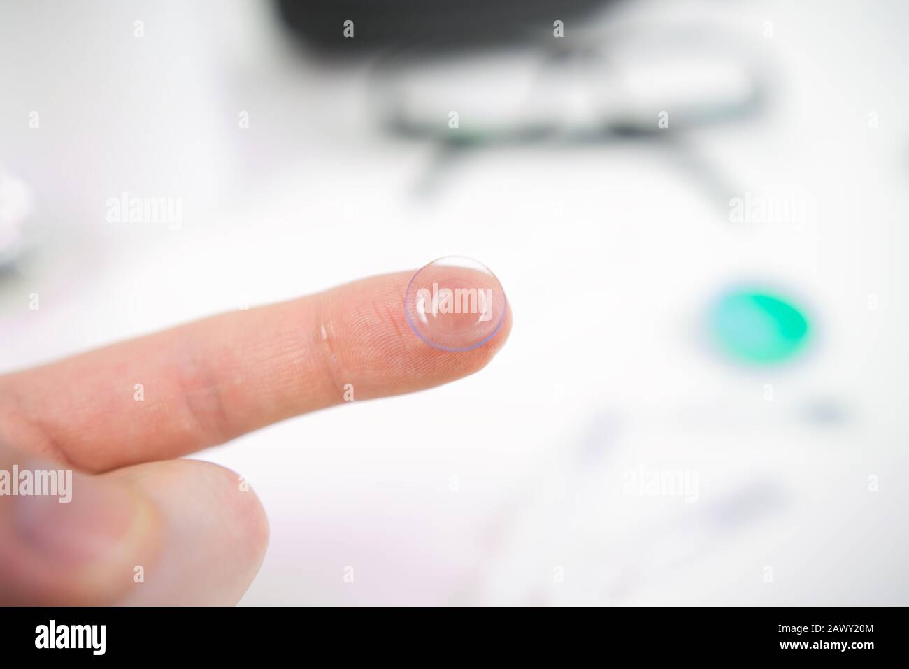 Hand mit Kontaktlinse, die in die Augen eingesetzt werden kann. Im Hintergrund sichtbare Brille, Tropfen und Hüllen Stockfoto