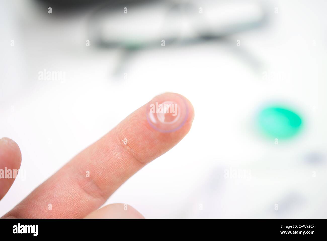 Hand mit Kontaktlinse, die in die Augen eingesetzt werden kann. Im Hintergrund sichtbare Brille, Tropfen und Hüllen Stockfoto